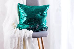 White plaid and green sequins pillow on gray armchair over window of living room